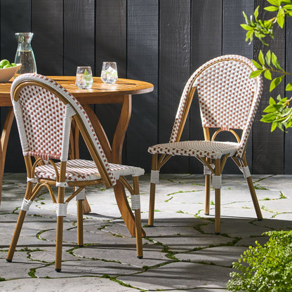 Two Outdoor Rattan and Aluminum French Bistro Chairs and a round table with glasses and a pitcher are arranged on a stone patio surrounded by greenery in gentle sunlight.
