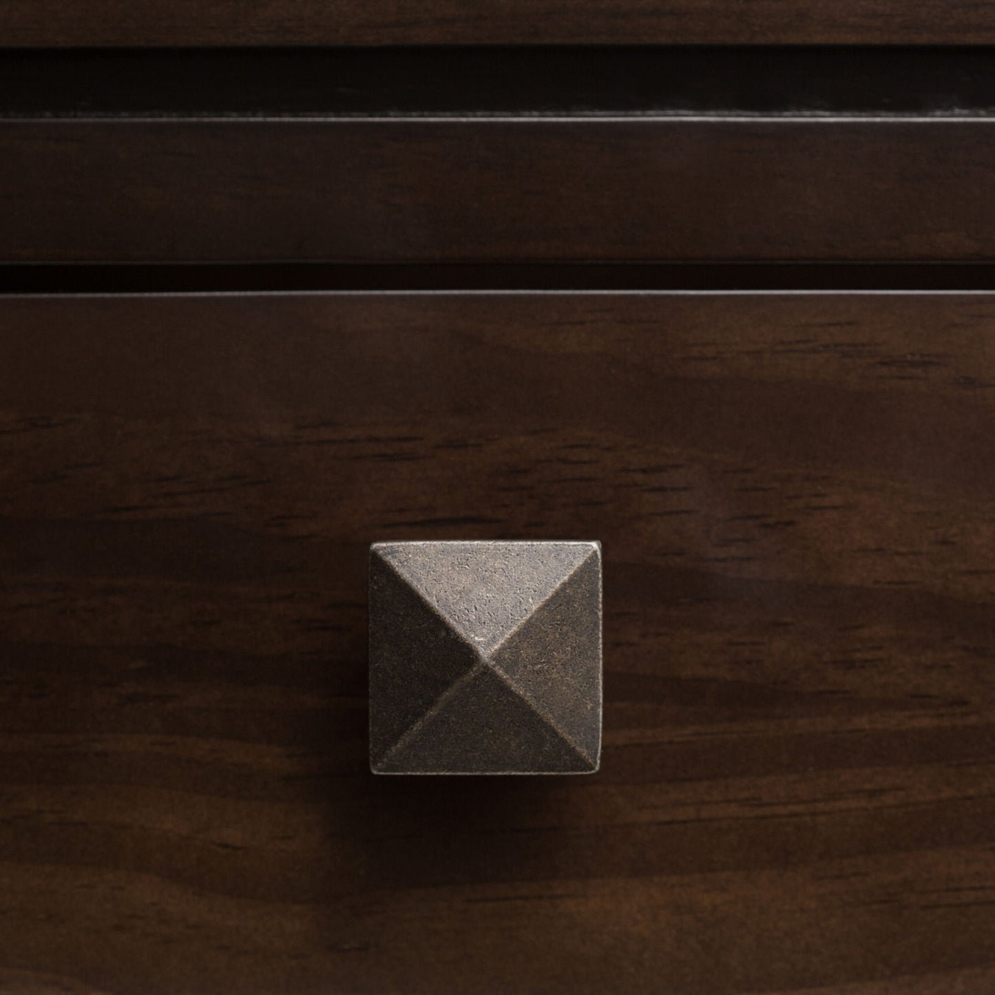 A close-up of the Cosmopolitan - Multipurpose Table featuring a square, metallic drawer knob with a pyramid-shaped design on a dark wooden drawer.