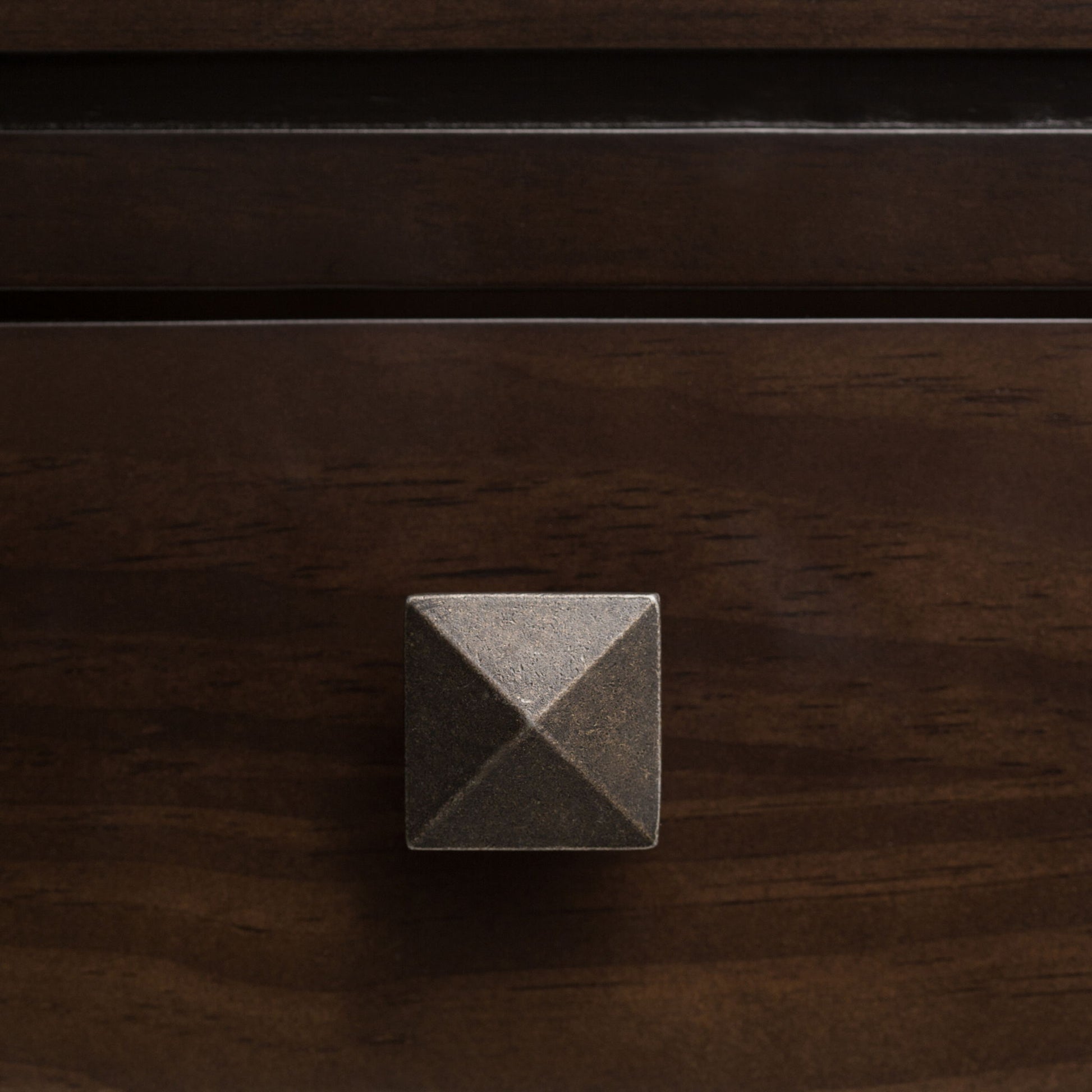 A close-up of the Cosmopolitan - Multipurpose Table featuring a square, metallic drawer knob with a pyramid-shaped design on a dark wooden drawer.