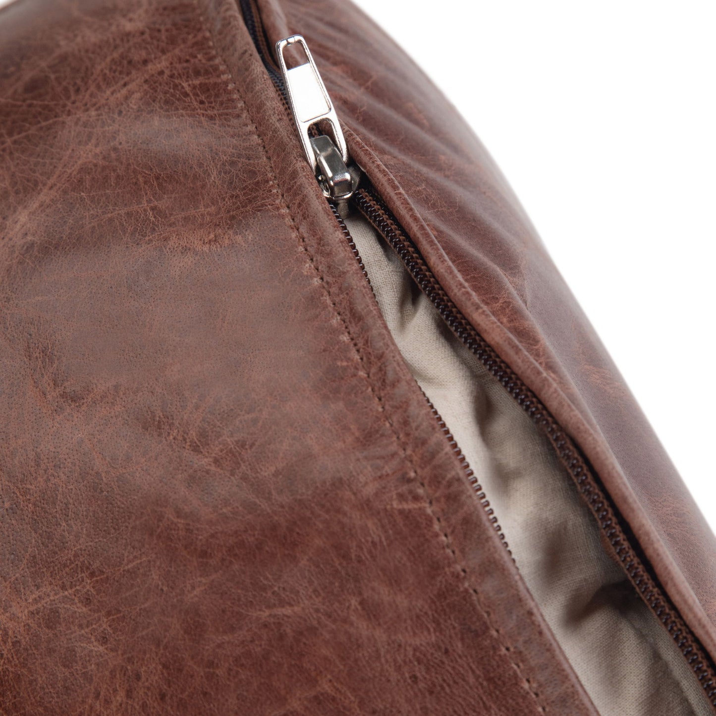 Close-up of the Connor - Handcrafted Round Pouf in brown leather with a silver zipper partially open, showing its light-colored fabric lining inside.