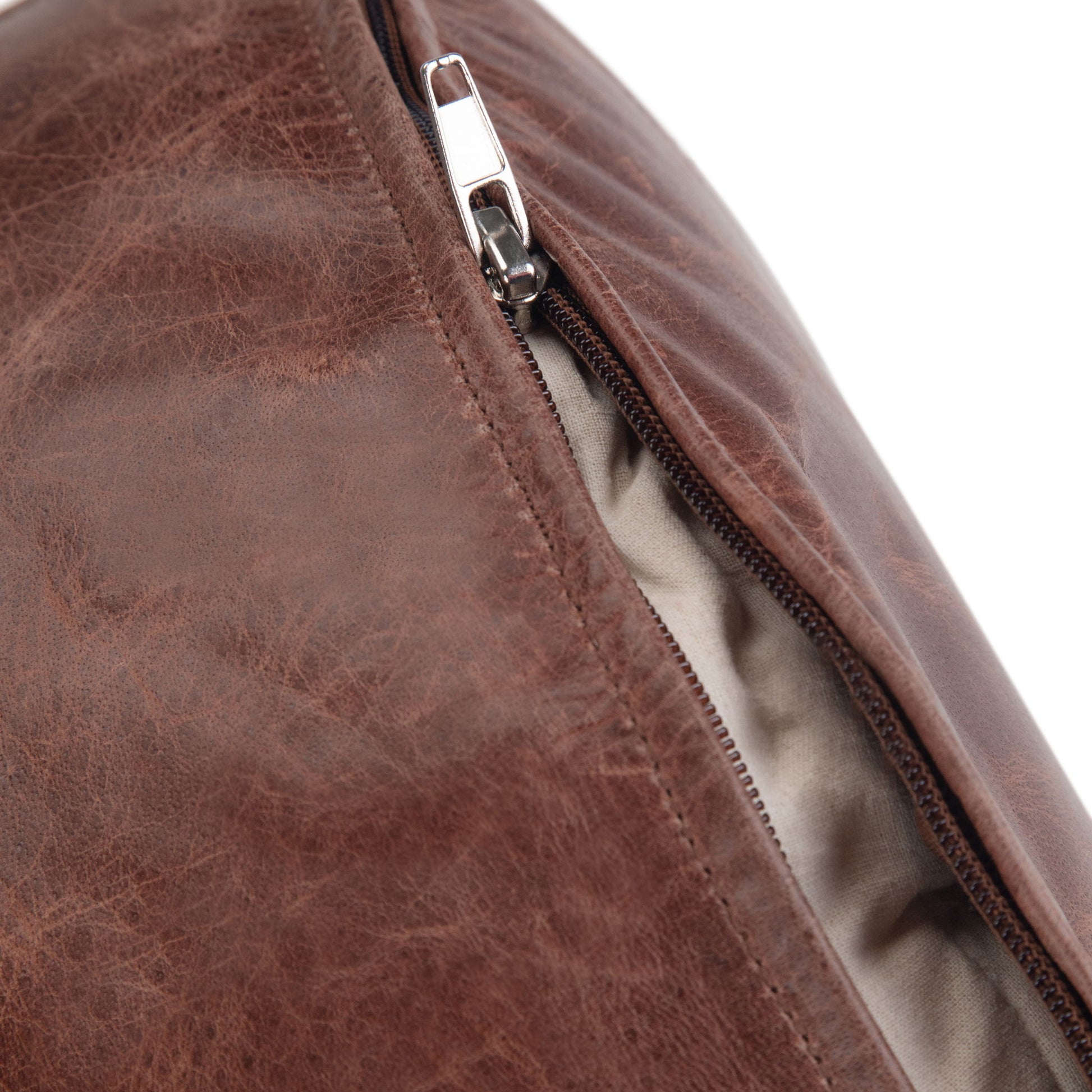 Close-up of the Connor - Handcrafted Round Pouf in brown leather with a silver zipper partially open, showing its light-colored fabric lining inside.