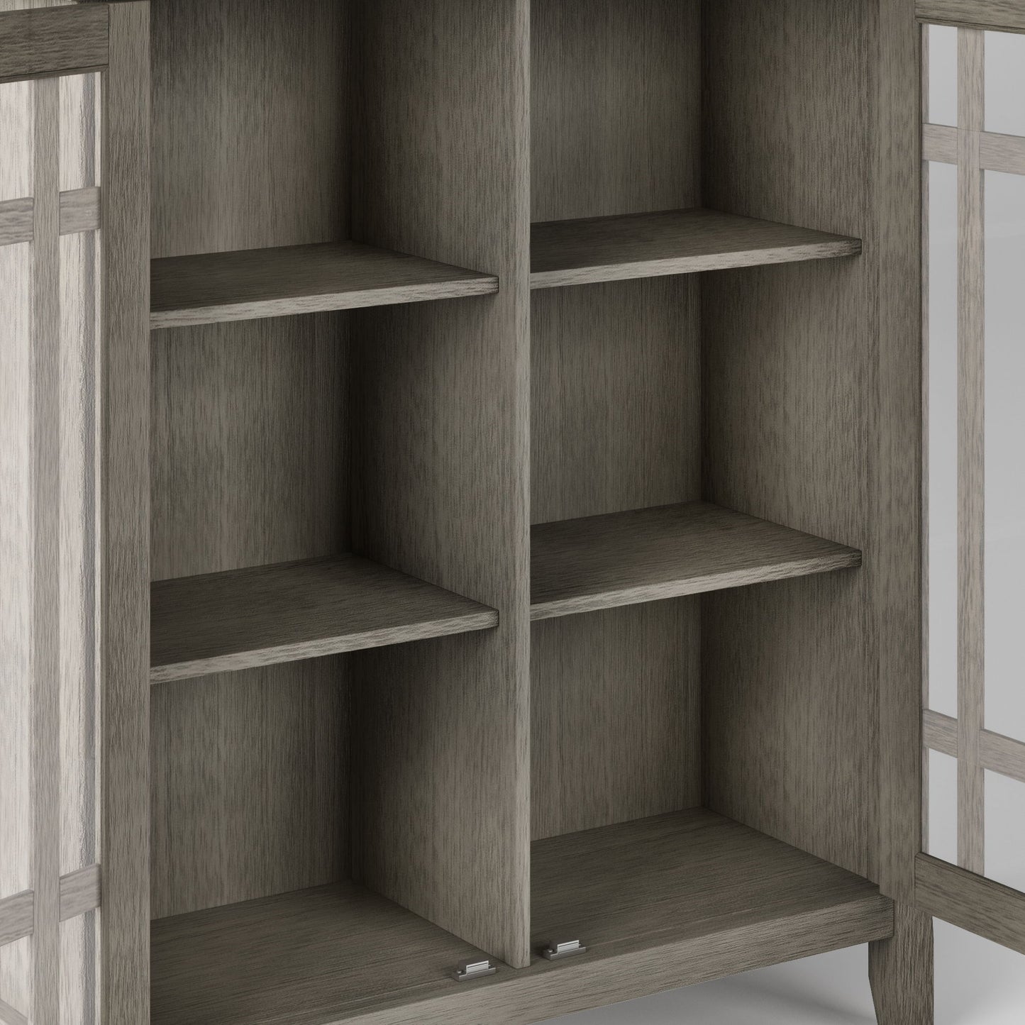A close-up of the Bedford Storage Media Cabinet shows four empty shelves in two sections. The partially visible doors have glass panels with wooden frames, and the cabinet features a grayish-brown wood finish.
