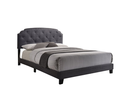 The Tradilla Queen Bed in gray features a modern upholstered design with a dark gray tufted headboard, silver nailhead trim, and is styled with striped bedding, pillows, and a matching dark gray throw blanket.