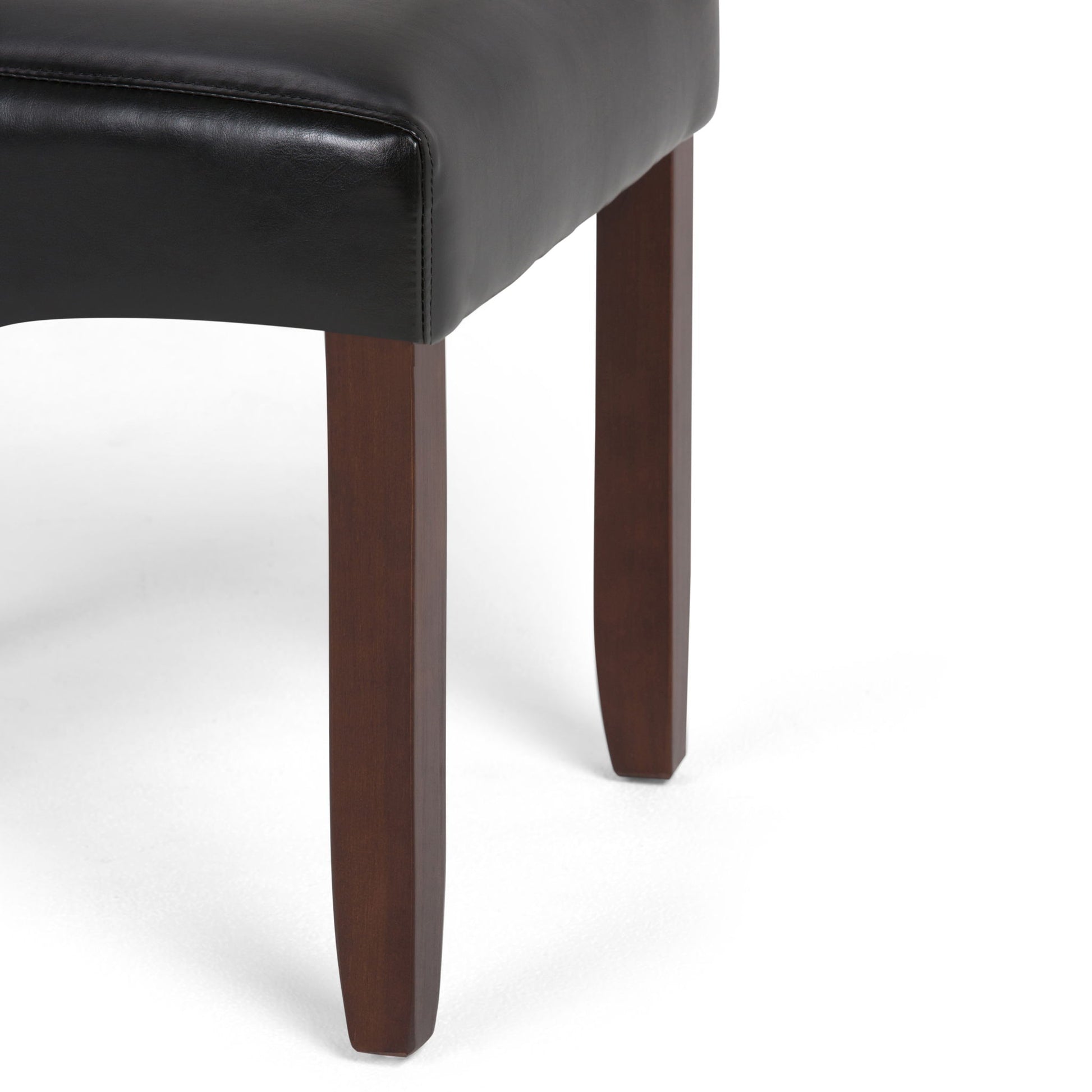 A close-up of the Cosmopolitan - Deluxe Tufted Parson Upholstered Chair (Set of 2) shows its dark brown wooden legs and black leather seat against a white background.