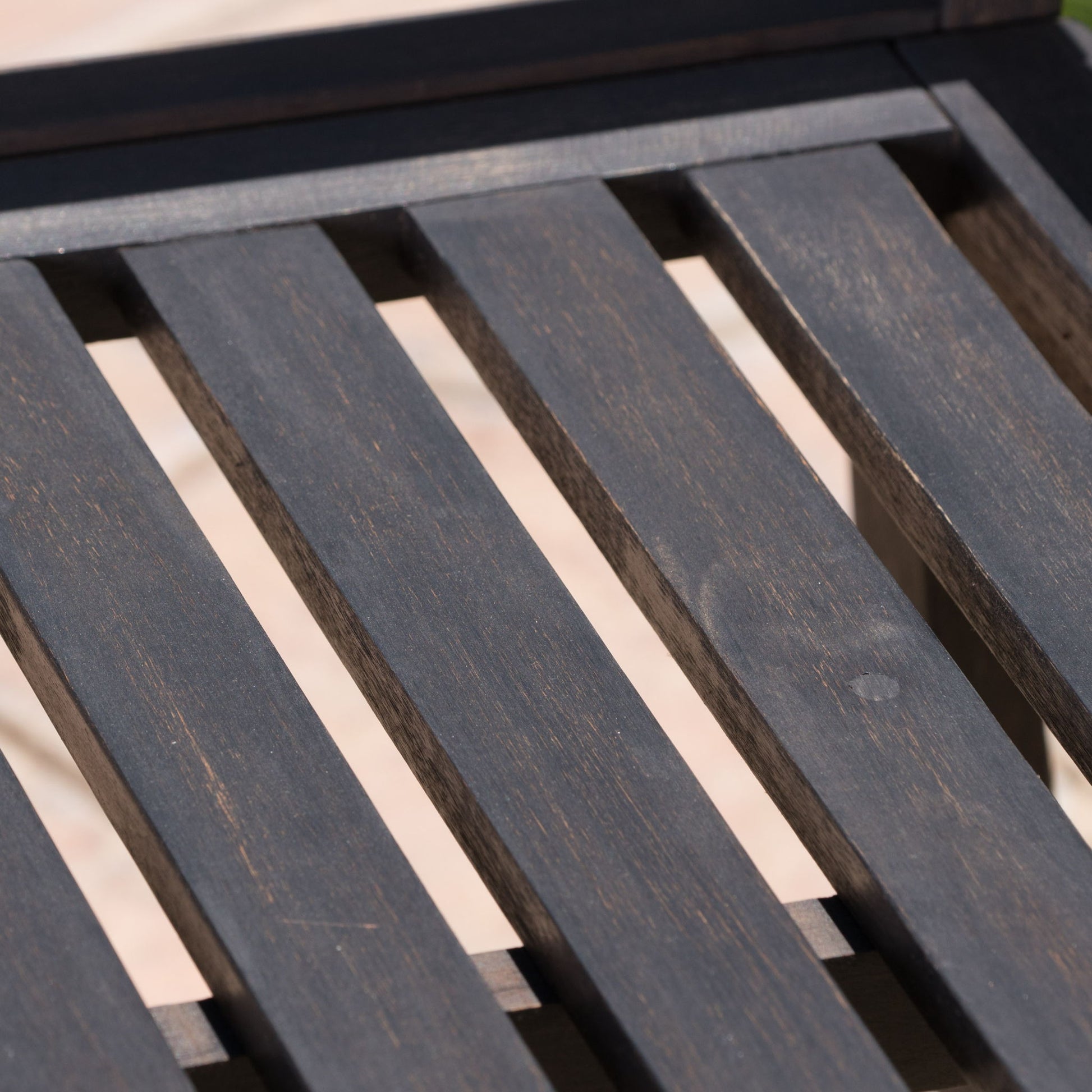 Close-up of the Farmhouse Style Loja Bench Indoor / Outdoor, featuring a dark wooden slatted surface with a slightly weathered texture and a softly blurred light background.