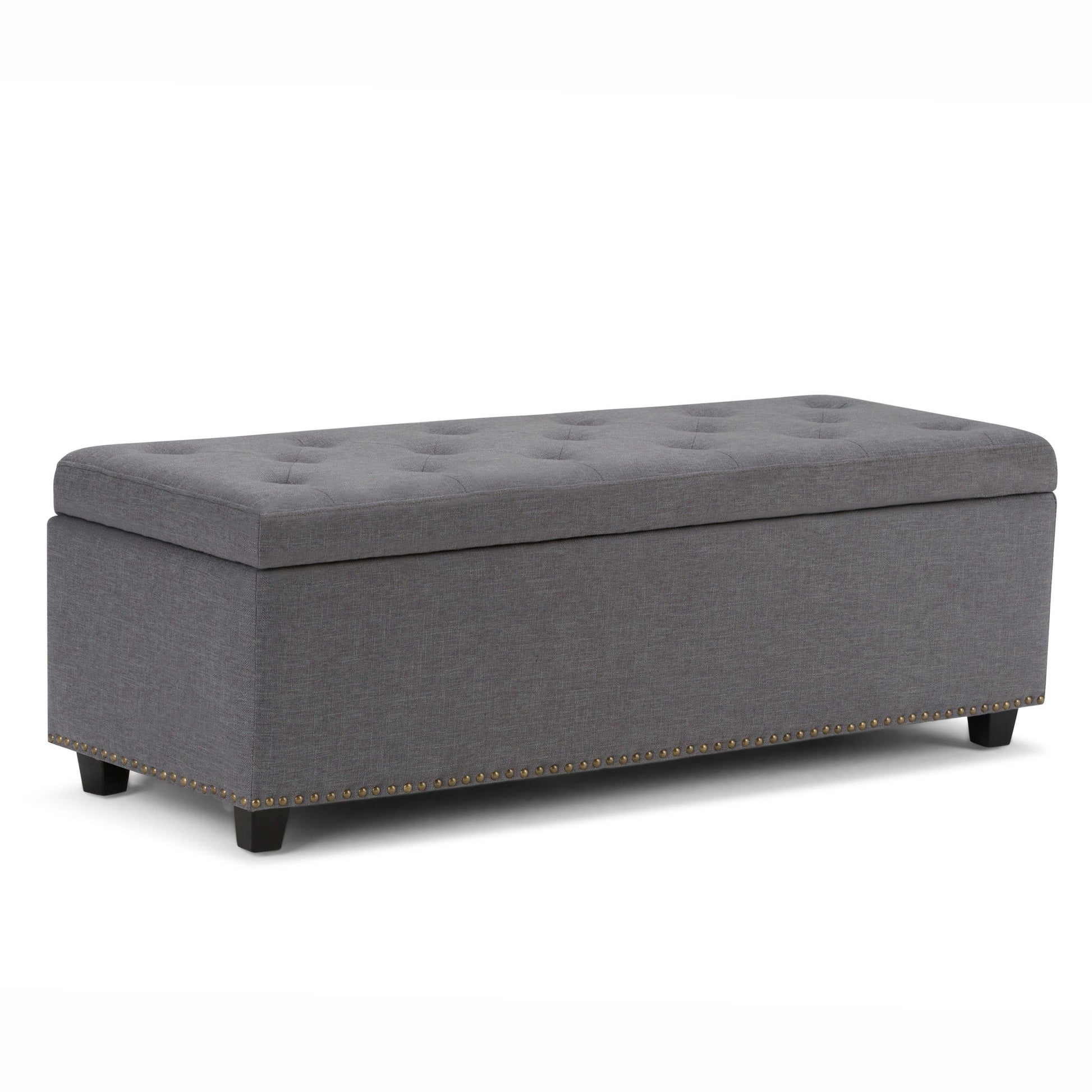 The Hamilton Upholstered Storage Ottoman features a gray tufted top, short black legs, and decorative brass nailhead trim along the bottom edge, shown on a white background.