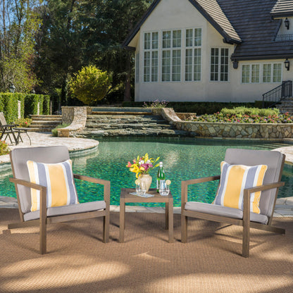 The Celestaria 3 Piece Outdoor Chat Set features two cushioned Adirondack chairs and a side table, arranged poolside in front of a spacious house with large windows and stone steps.