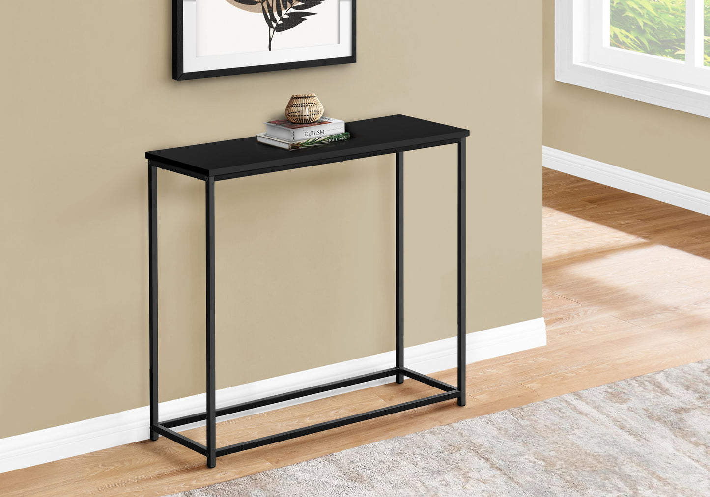 The Accent Console Table For Entryway offers stable support and a contemporary look with its slim black metal frame and rectangular top. Against a beige wall, it displays decor and a book beneath natural light from a nearby window.