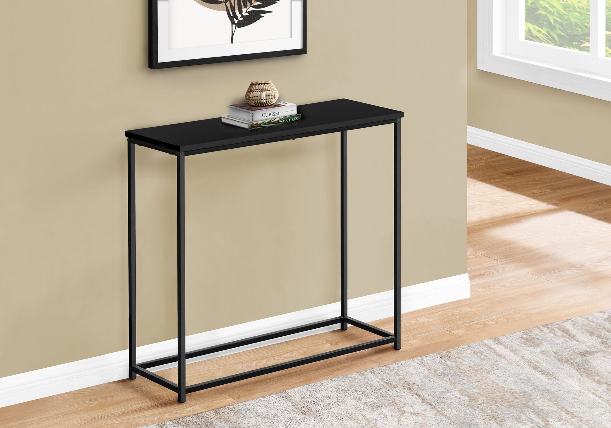 The Accent Console Table For Entryway offers stable support and a contemporary look with its slim black metal frame and rectangular top. Against a beige wall, it displays decor and a book beneath natural light from a nearby window.