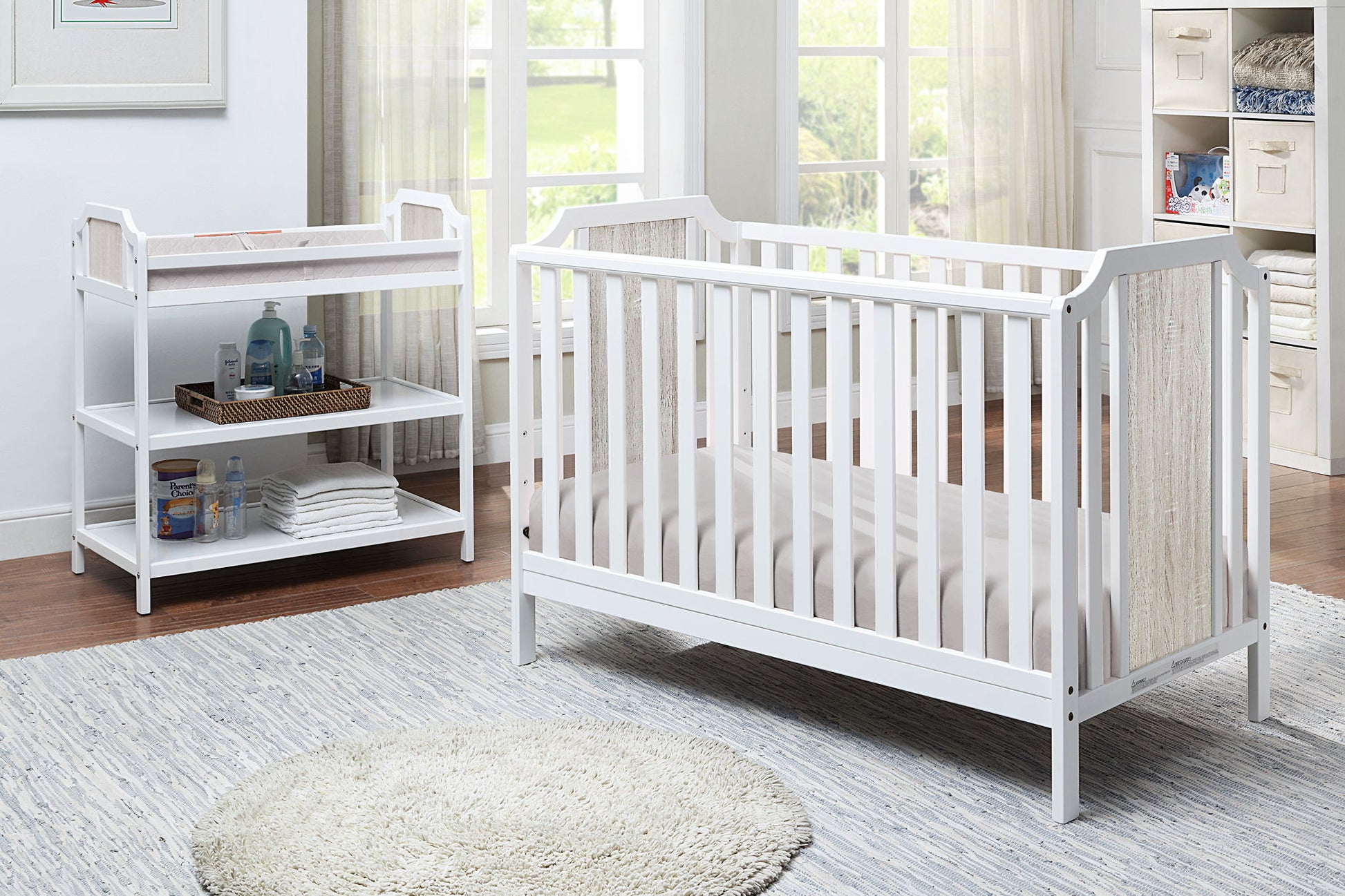 Bright nursery room featuring a white crib and the Brees Changing Table, shelves with baby essentials, a round rug on the floor, and large windows filling the space with natural light.
