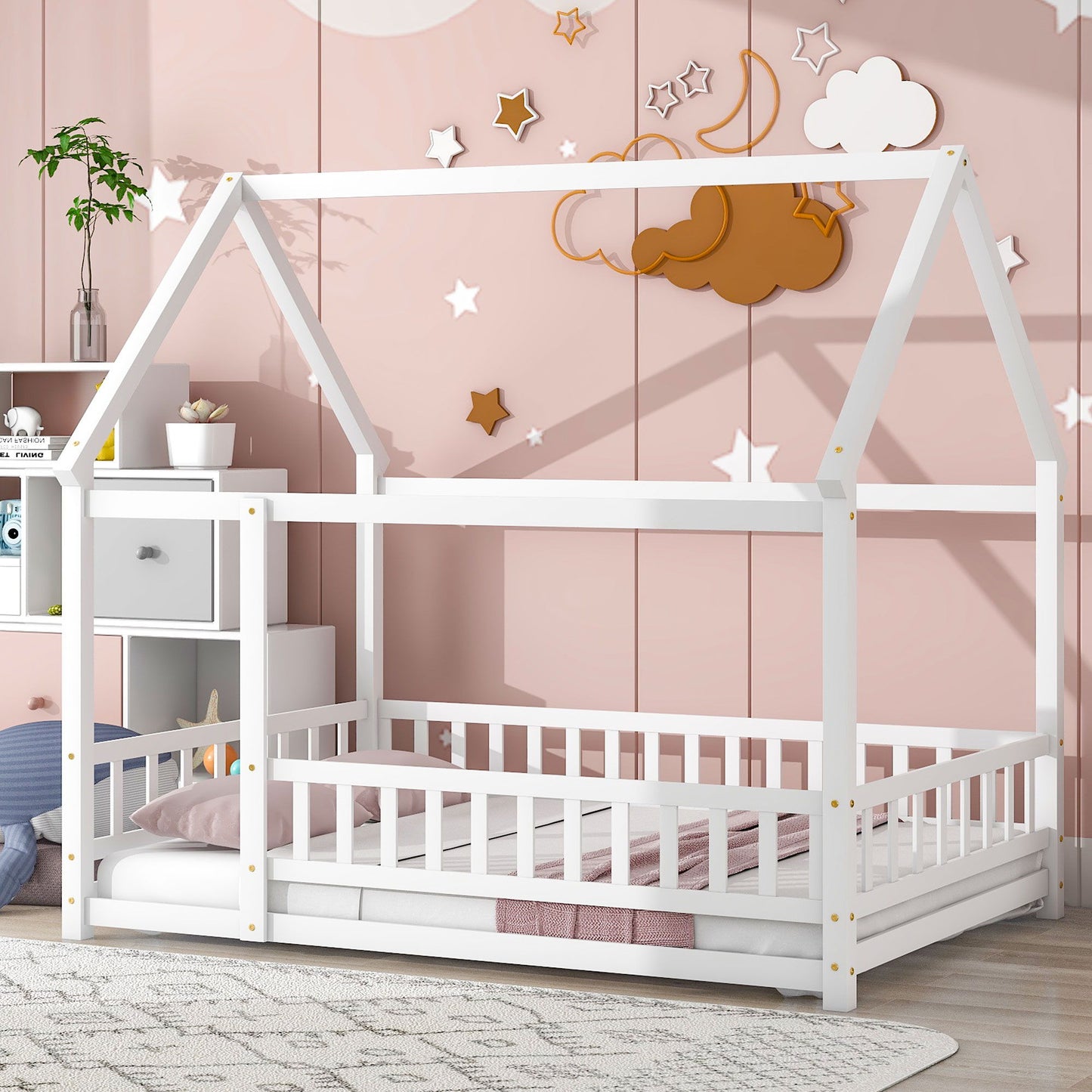 A pink-themed kids' room features the Floor Wooden Bed With House Roof Frame and Fence Guardrails in white. Above the bed are star and cloud wall decorations, with shelves nearby displaying toys and decor.