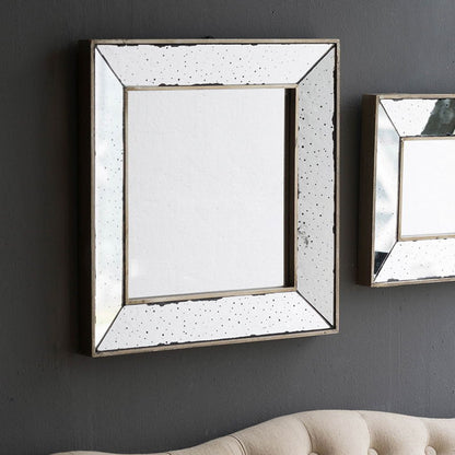 A Distressed Accent Mirror, Traditional Style Framed Wall Mirror for Living Room, with a wide distressed frame, hangs on a dark gray wall above a beige tufted sofa. Another similar mirror is partially visible to the right.