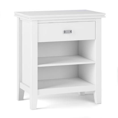 The Artisan - Handcrafted Bedside Table features a white wooden finish, single top drawer with square metal handle, two open shelves below, and a modern design with clean lines and slightly tapered legs.