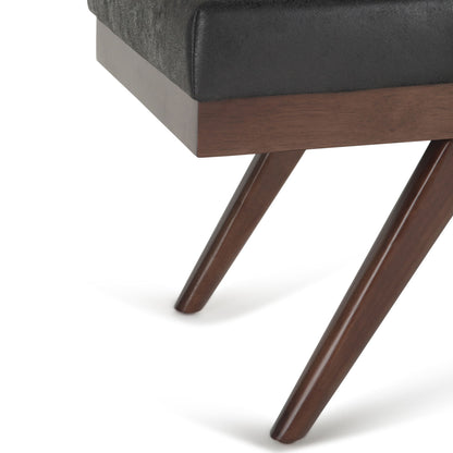 Close-up of the Chanelle Mid-Century Ottoman Bench, featuring a dark wood tapered leg, black upholstered cushioned seat, and wooden frame.