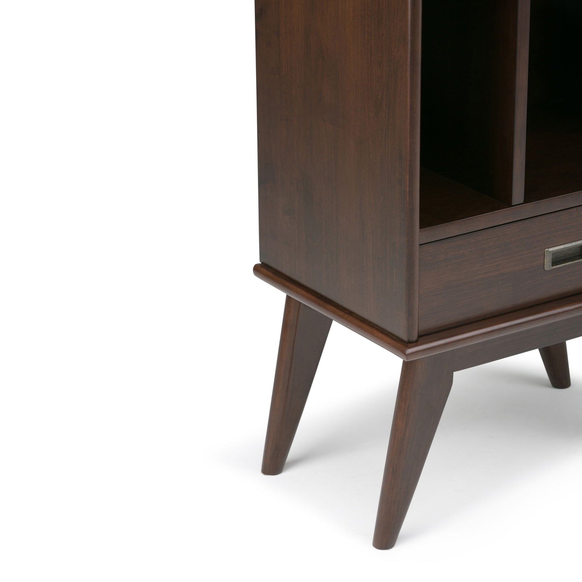 The image shows the lower corner of the Draper - Mid Century Wide Bookcase And Storage Unit, featuring dark wood, angled tapered legs, an open shelf, and a partial drawer with a metal handle.