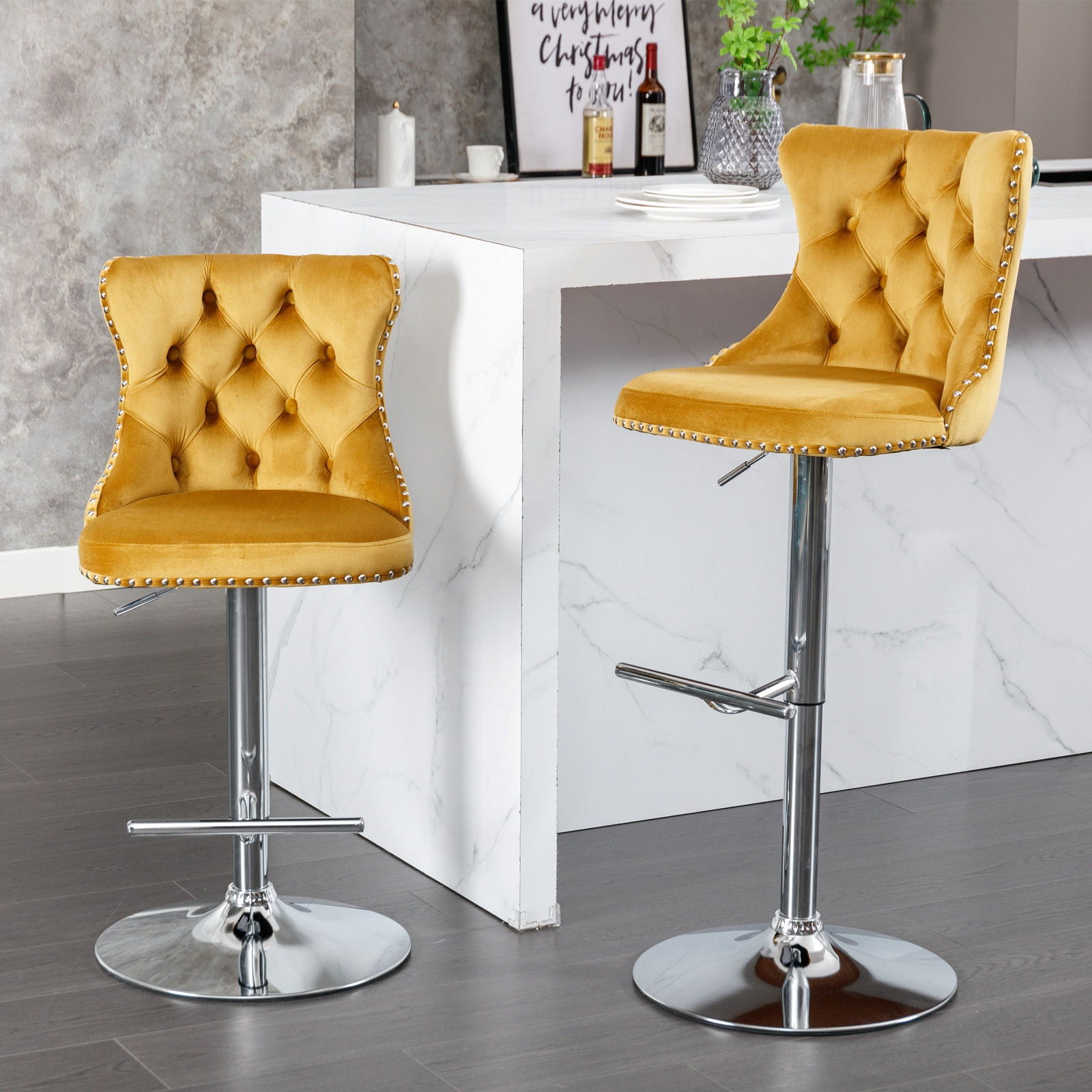 A set of two modern Swivel Velvet Barstools with mustard yellow tufted seats, adjustable chrome bases, and backs stand beside a white marble kitchen counter on a gray floor.