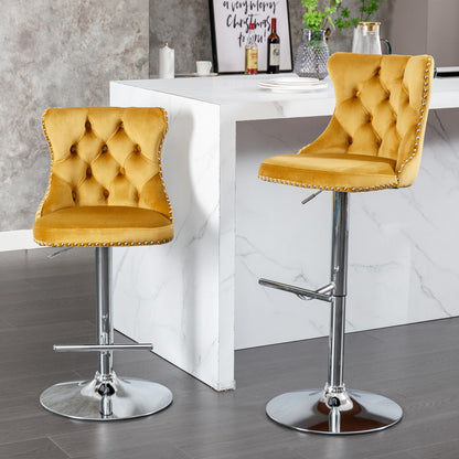 A set of two modern Swivel Velvet Barstools with mustard yellow tufted seats, adjustable chrome bases, and backs stand beside a white marble kitchen counter on a gray floor.