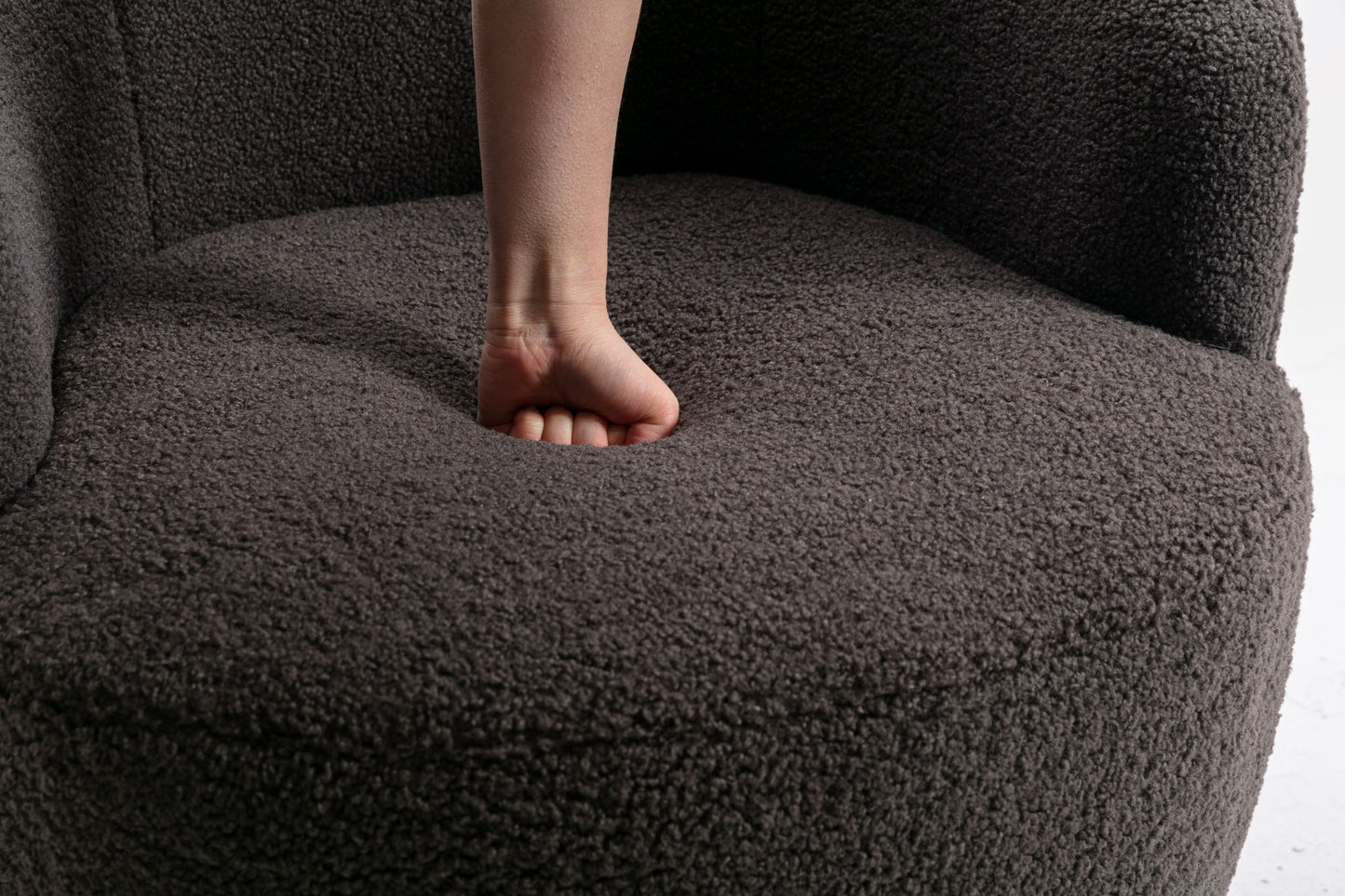 A person's fist presses firmly into the seat of the Teddy Fabric Swivel Accent Armchair Barrel Chair With Powder Coating Metal Ring, creating a noticeable indentation in its soft, textured cushion.