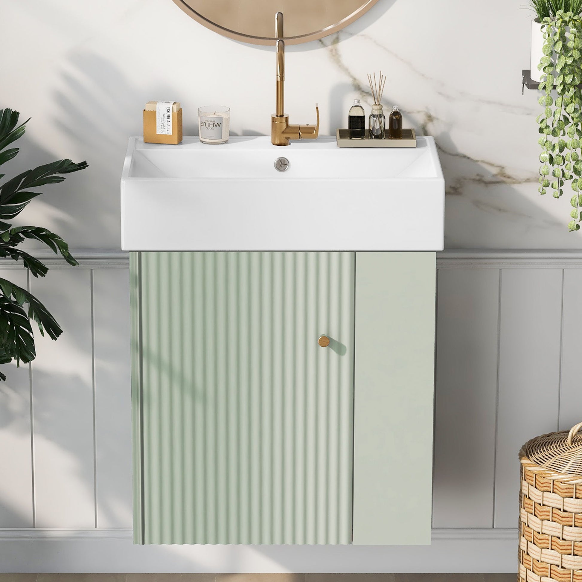 The Modern Floating Bathroom Vanity With Ceramic Basin, featuring a gold faucet, ribbed light green cabinet, and round mirror, is accented by decor like candles and plants against a gray and marble wall—ideal for small bathrooms.