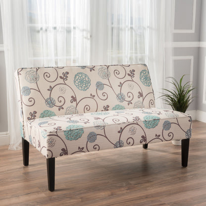 A Contemporary Loveseat With Upholstered Fabric and birch wood legs is placed on a wooden floor in a bright room with light gray walls, white trim, sheer curtains, and a potted plant in the corner.