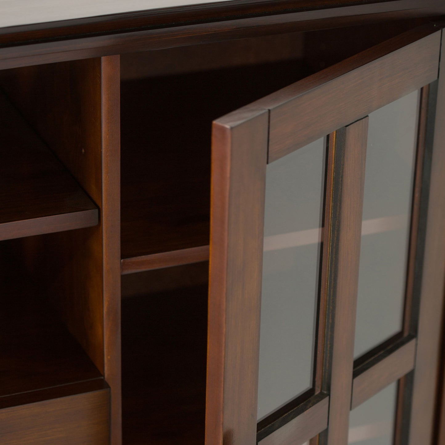A close-up view of the Artisan Handcrafted Tall TV Media Stand shows its dark brown wood with glass-paneled doors, one partially open to reveal empty shelves inside.