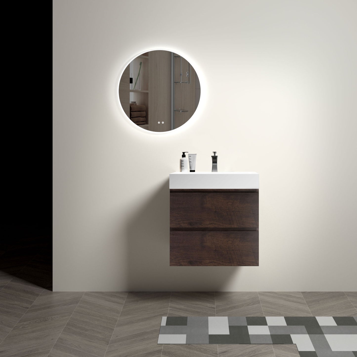 A minimalist bathroom features the Alice wall-mounted vanity with a one-piece white sink. A round, backlit mirror hangs above, three toiletries rest on the vanity, and patterned tiles accentuate the floor.