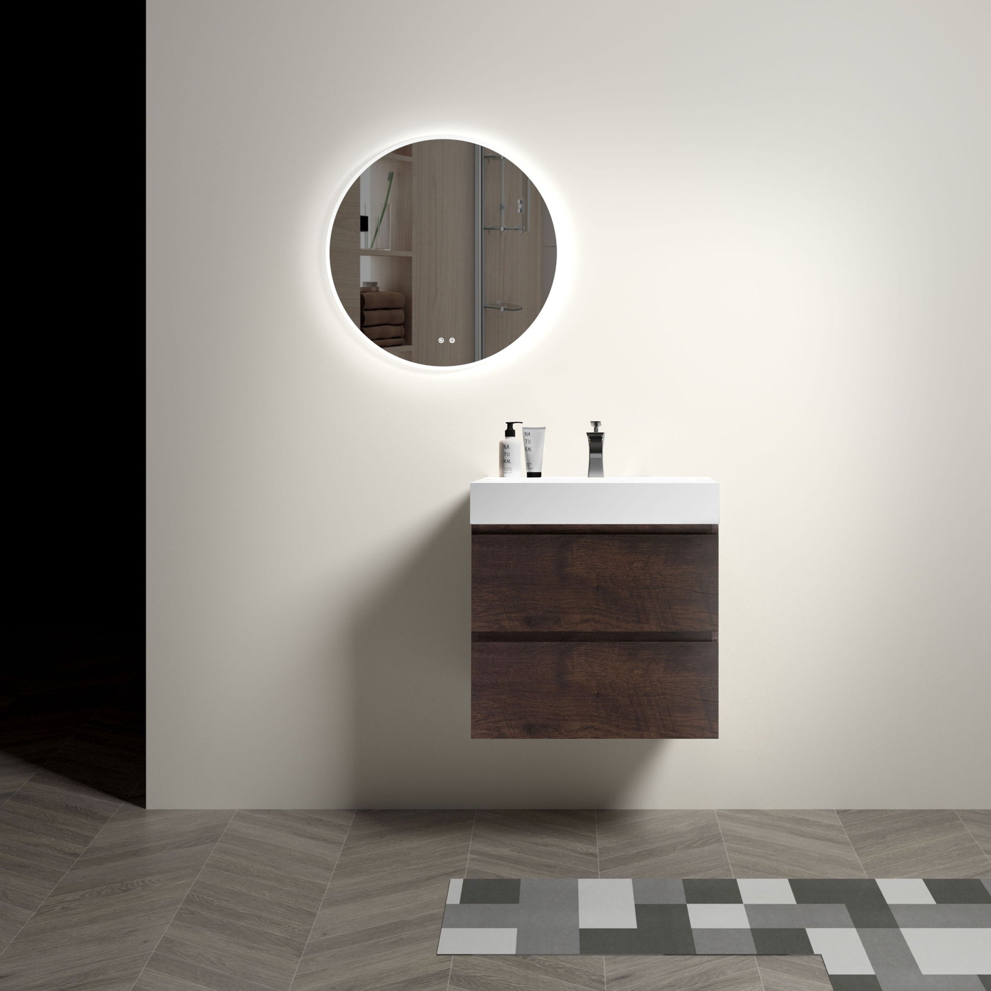 A minimalist bathroom features the Alice wall-mounted vanity with a one-piece white sink. A round, backlit mirror hangs above, three toiletries rest on the vanity, and patterned tiles accentuate the floor.