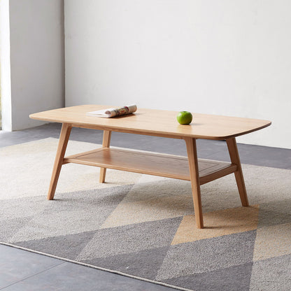 The Low Coffee Table With Storage Shelf stands on a geometric-patterned rug, displaying a rolled-up magazine and green apple. Behind it is a plain white wall and tiled floor.