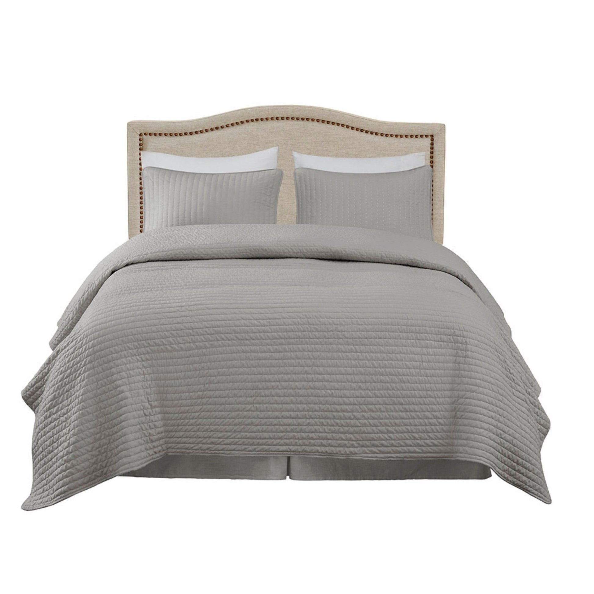 A neatly made bed features the Elegant Panel Headboard with copper nailheads and adjustable metal legs, complemented by two gray pillows and a matching gray quilted bedspread draped over the sides.