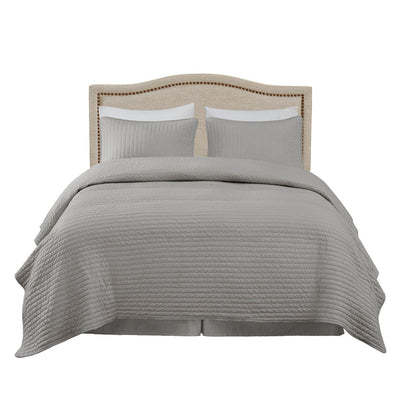 A neatly made bed features the Elegant Panel Headboard with copper nailheads and adjustable metal legs, complemented by two gray pillows and a matching gray quilted bedspread draped over the sides.