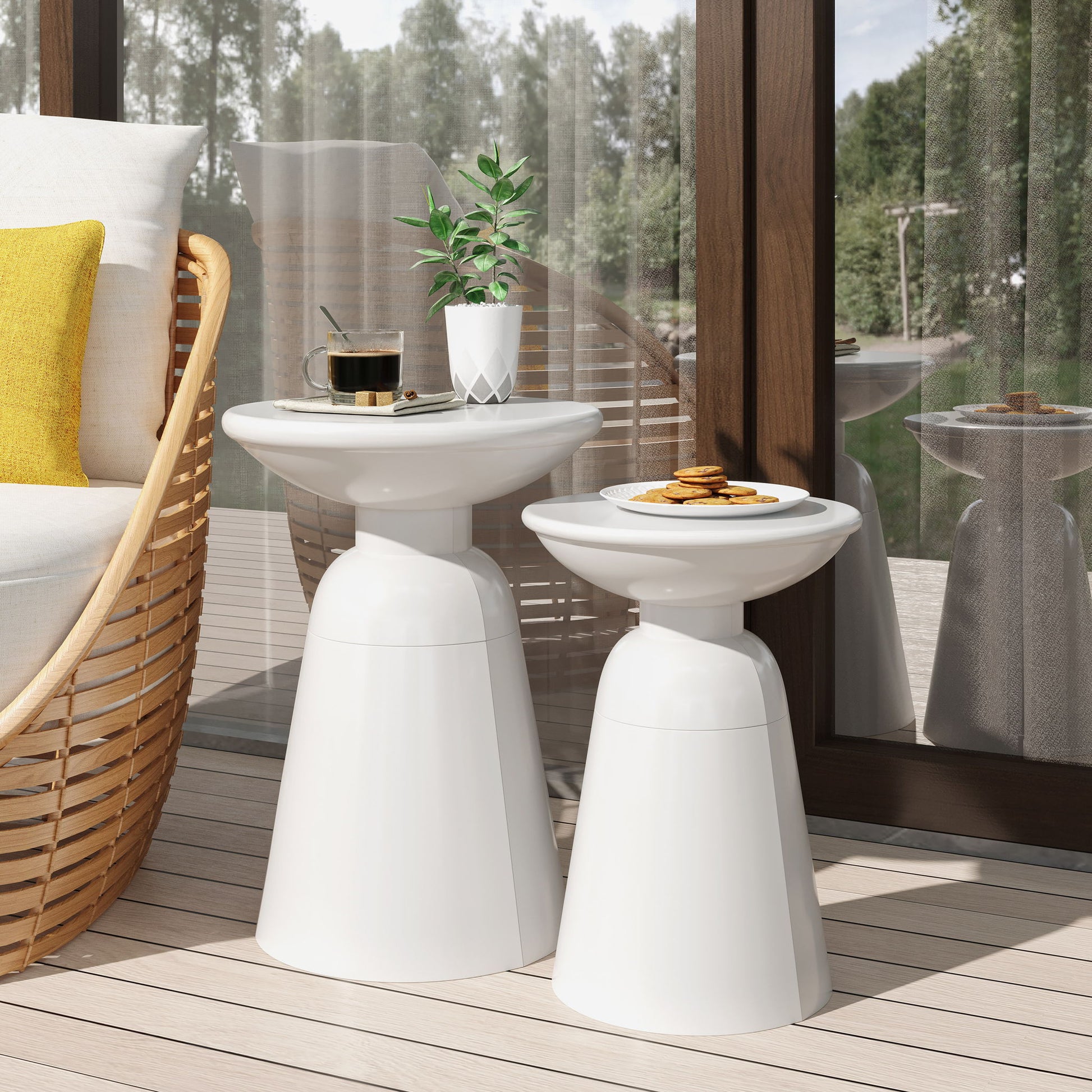 Two Serenita - Outdoor Side Tables With Flared Design (Set of 2) sit on a patio, one holding coffee and a plant, the other cookies, beside a wicker chair with yellow and white cushions near a large reflective window.