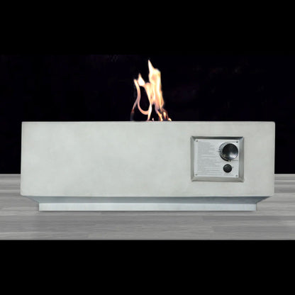 The Reinforced - Propane / Gas Fire Pit Table features a sleek, rectangular design with a visible right-side control panel and flames on top, displayed against a dark backdrop on a light wood floor.