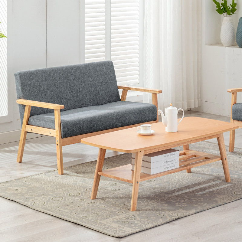 The Bahamas - Living Room Set features a light wood coffee table, gray cushioned wooden-arm sofa, patterned rug, tea set, white blinds and curtains, and decorative vases for a modern living room look.