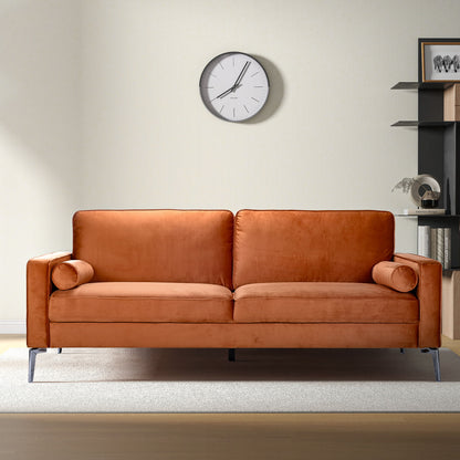 A modern living room featuring the Axten - Sofa - Orange with two matching bolster pillows, a light rug, a wall clock, and black shelves with decor against a cream-colored wall.