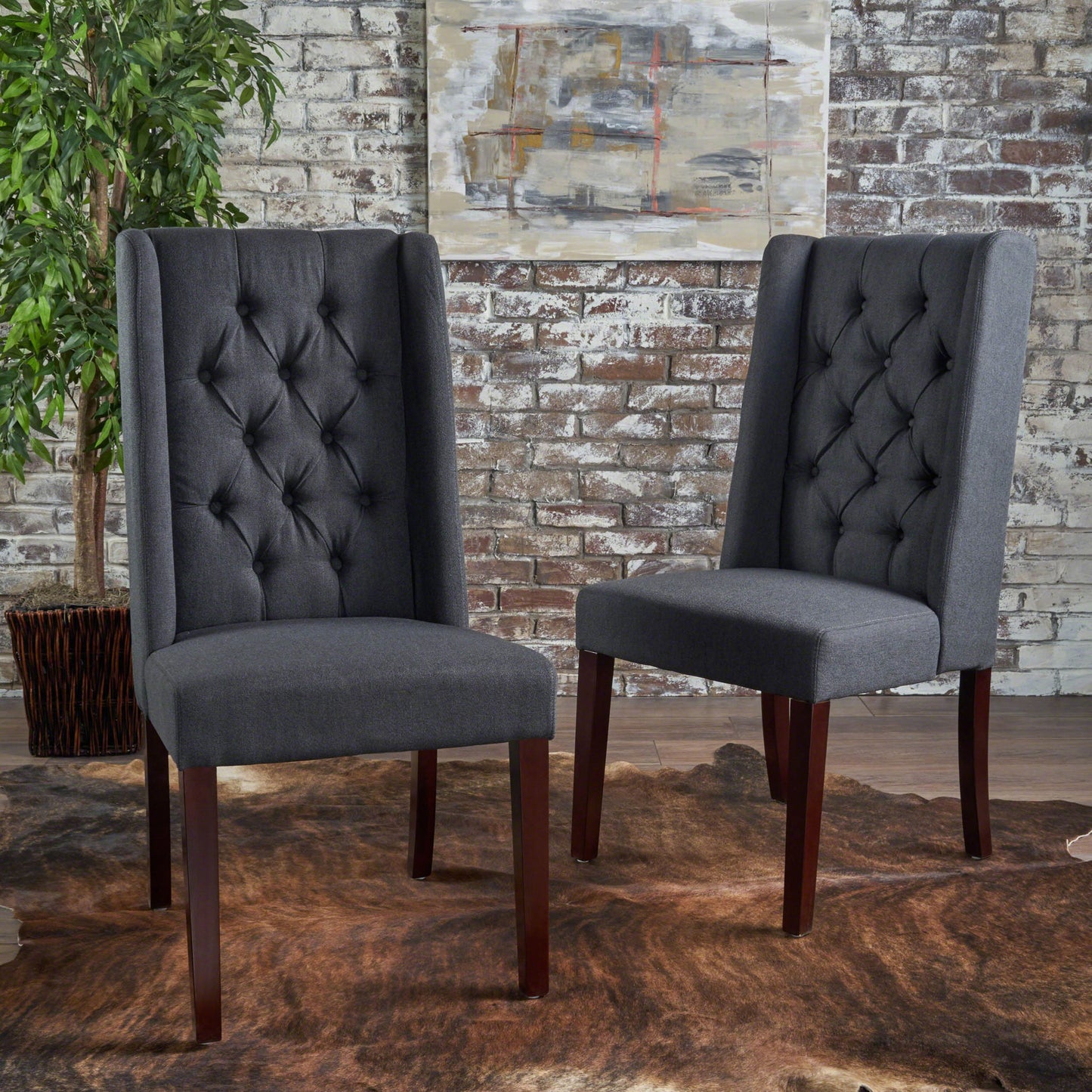 A pair of Sophisticated Tufted Dining Chairs with high backs and wooden legs are placed on a brown fur rug before a whitewashed brick wall, accented by a leafy potted plant and abstract art in the background.
