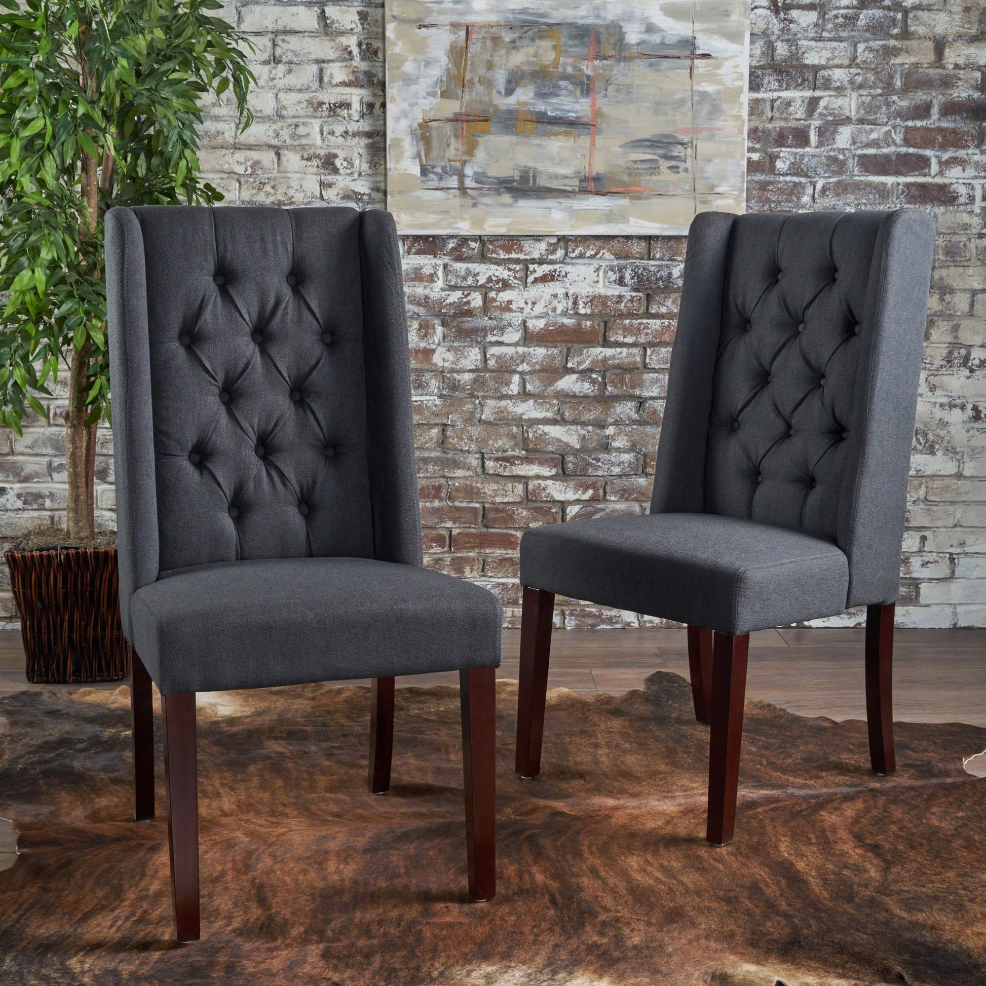A pair of Sophisticated Tufted Dining Chairs with high backs and wooden legs are placed on a brown fur rug before a whitewashed brick wall, accented by a leafy potted plant and abstract art in the background.