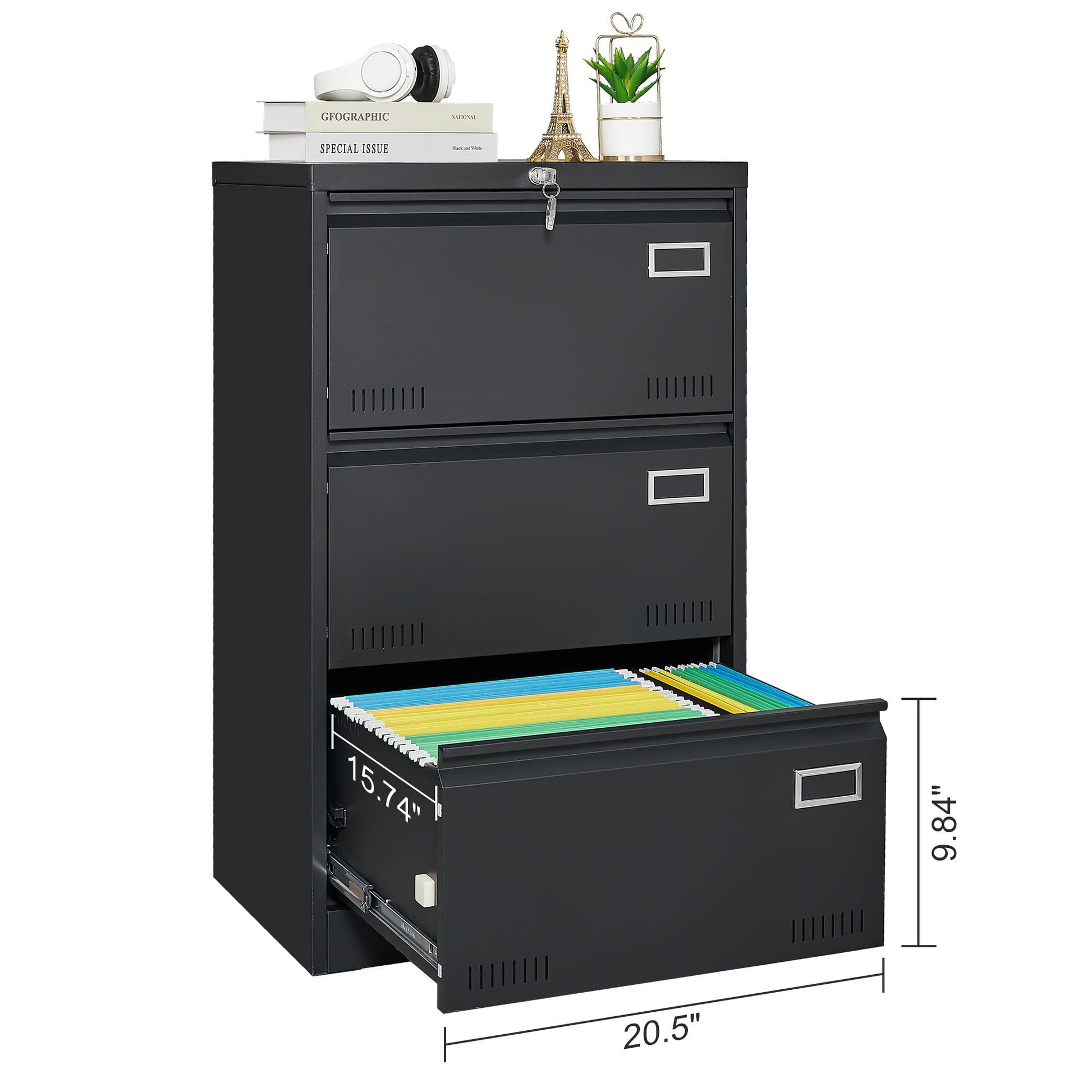 The Filing Cabinet Lateral File Cabinet 3 Drawer features one open drawer with organized folders, a top surface holding a book, headphones, an Eiffel Tower decor, and a plant. Its labeled dimensions suit home or office use and include lockable drawers.