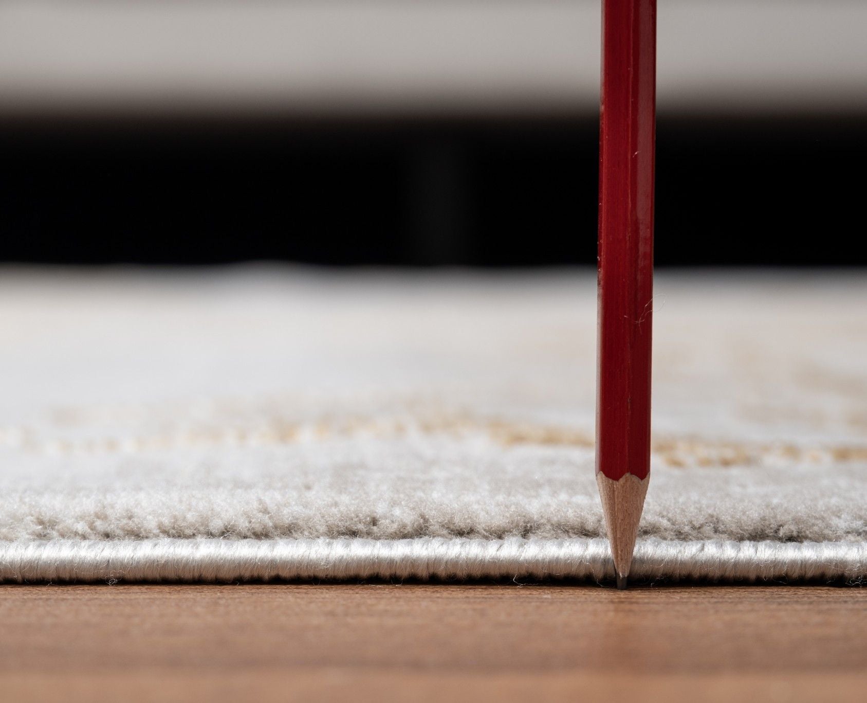 A close-up of the Elegance - GC_CNC6004 Area Rug with a red pencil standing vertically, highlighting the rug’s thickness above a wooden floor.