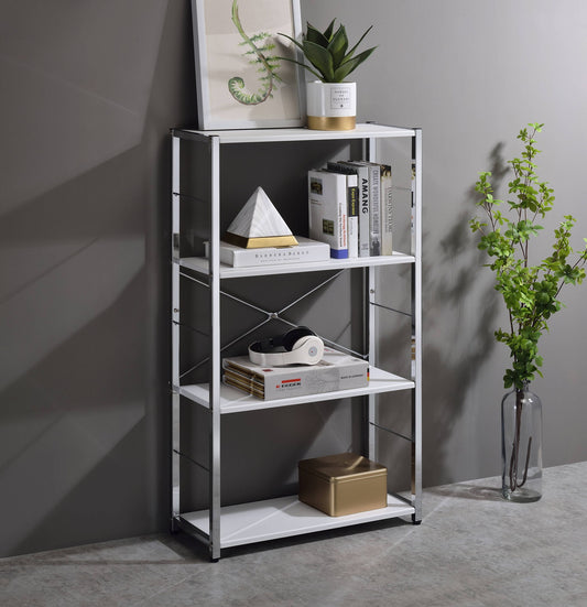 The Tennos - Bookshelf - White features four shelves for books, decor, a potted plant, and headphones. On top sit a framed artwork and plant, while a vase with green branches stands nearby against the gray wall.
