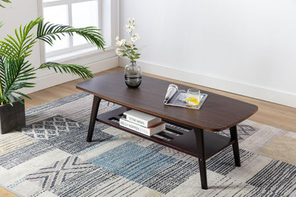 The Bahamas - Coffee Table holds a glass vase with flowers, a magazine, and a drink on top. Books are stored on its lower shelf. The table sits on a patterned rug by the window next to a potted plant.