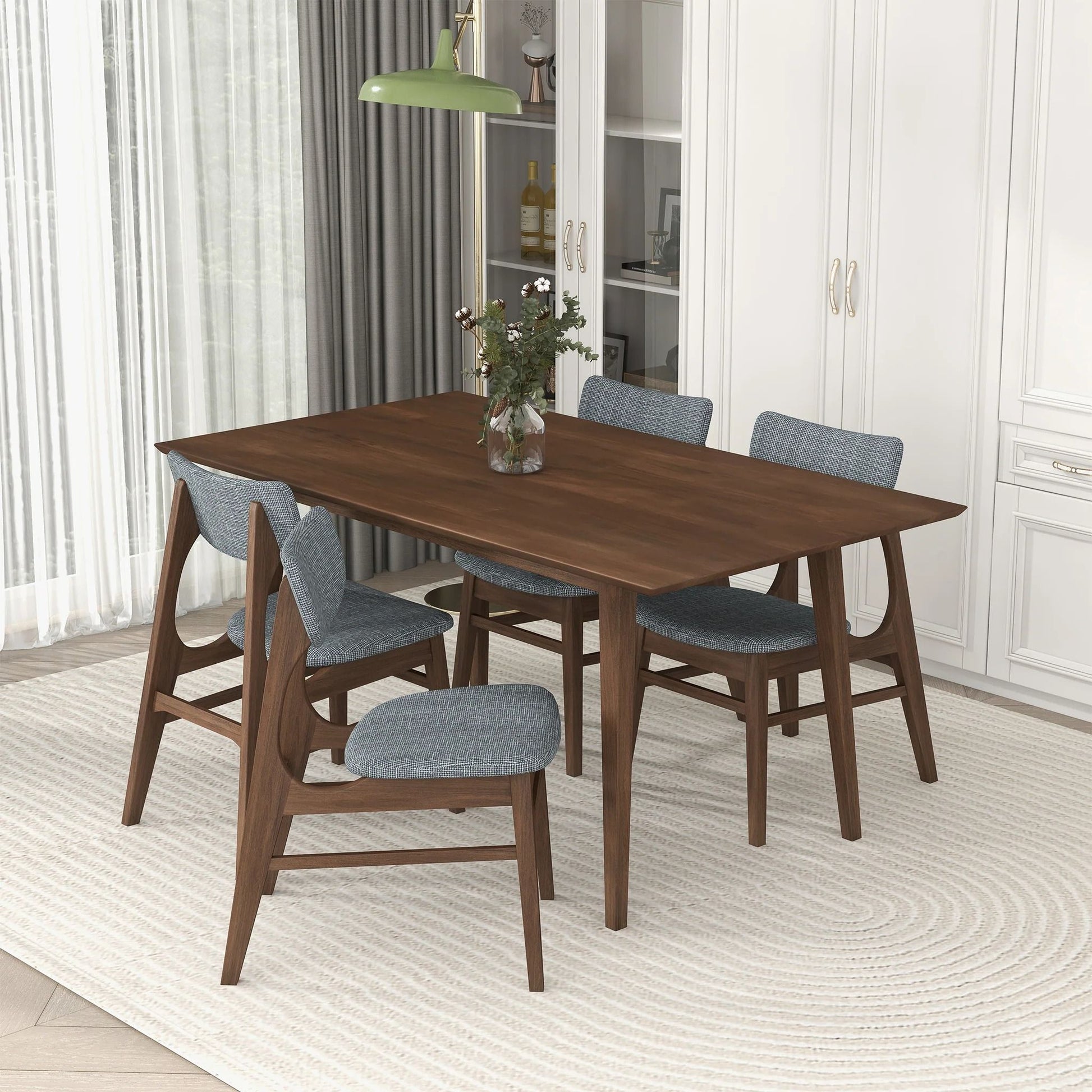 The Levi - Modern Style Rectangular Dining Kitchen Table sits on a light textured rug, surrounded by four blue upholstered chairs in a bright, modern room with white cabinets and curtains and a vase of flowers as décor.