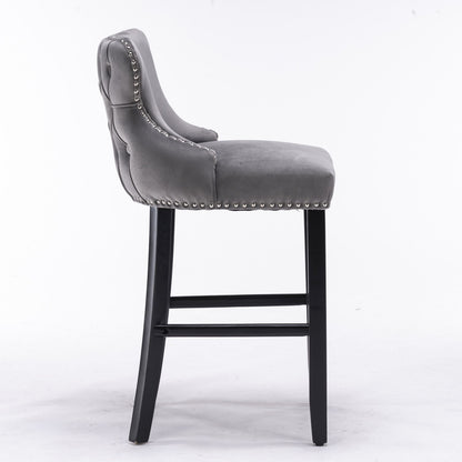 A set of 2 contemporary velvet wing-back barstools with button tufting, chrome nailhead trim, and wooden legs, shown in profile on a white background.