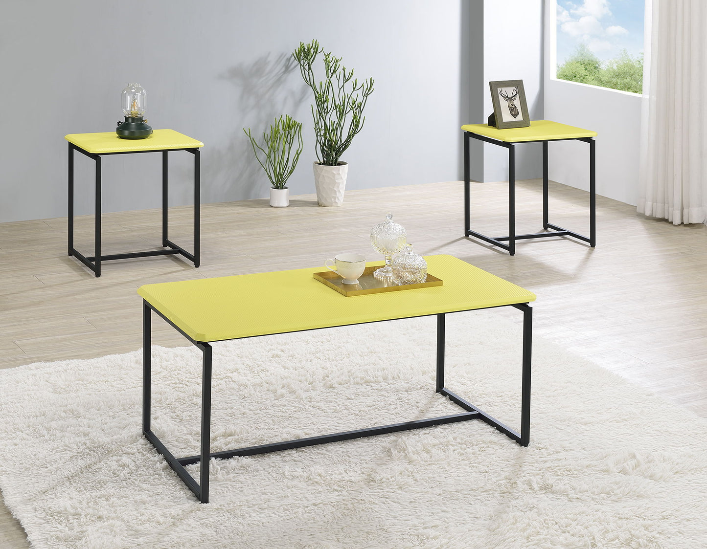 A modern living room features the GT - 3 Piece Carbon Fiber Wrap Coffee Table And End Table set in yellow with black metal frames, topped with decorative items and plants. A window lets in sunlight for a bright, inviting scene.