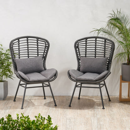 Two Calypso outdoor chairs with water-resistant gray cushions and iron frames sit on a tile floor by a white wall, surrounded by green potted plants for a cozy, inviting setting.