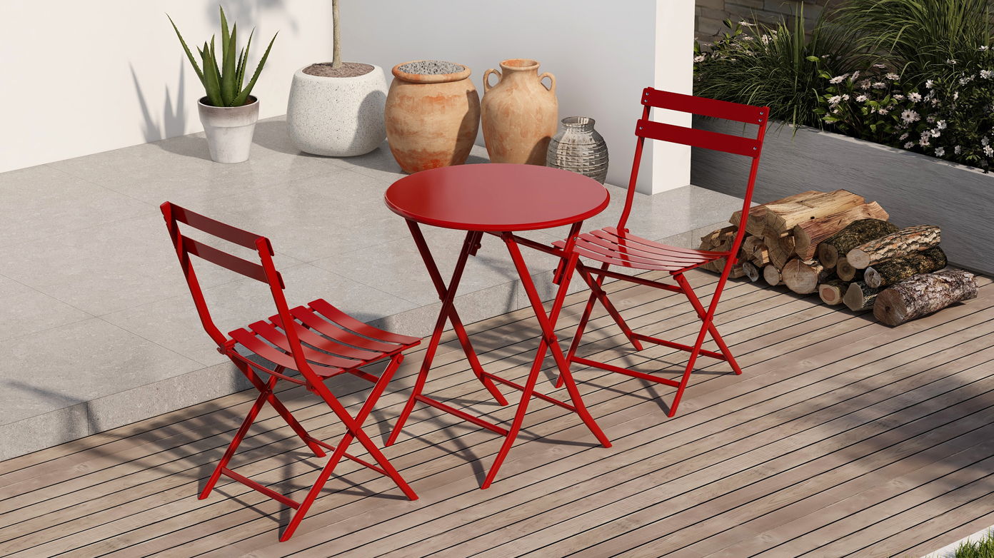 The 3 Piece Patio Bistro Set of a foldable round table and two chairs in red is placed on a wooden deck, surrounded by potted plants, large decorative vases, and a stack of firewood.