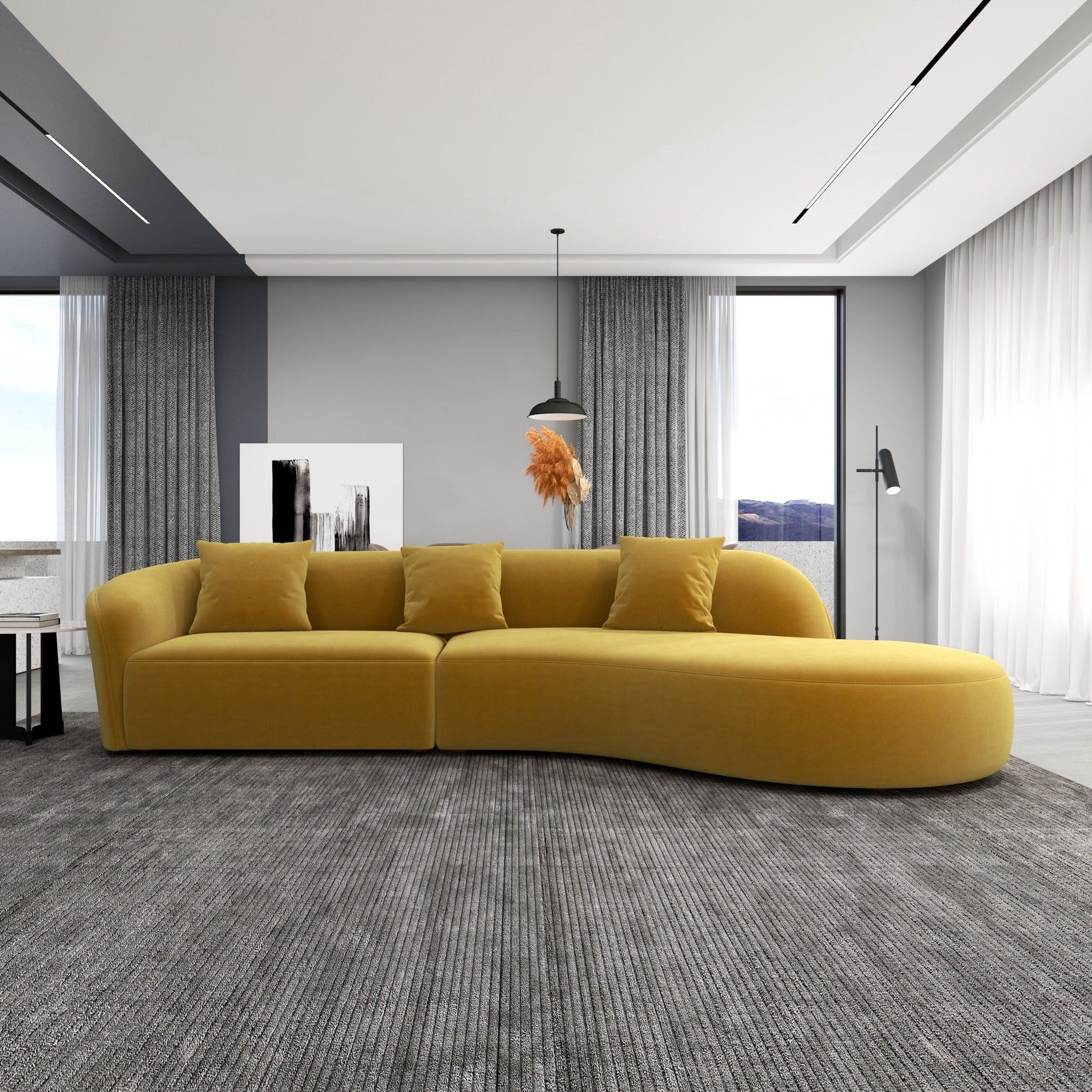 A modern living room featuring the Elijah - Japandi Style Curvy Sectional Sofa in yellow, a gray area rug, floor-to-ceiling windows with sheer curtains, a pendant light, floor lamp, and abstract art on gray walls.