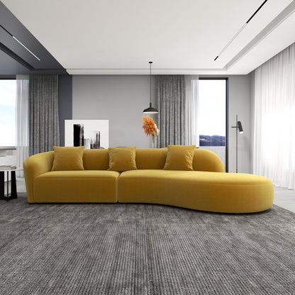 A modern living room featuring the Elijah - Japandi Style Curvy Sectional Sofa in yellow, a gray area rug, floor-to-ceiling windows with sheer curtains, a pendant light, floor lamp, and abstract art on gray walls.