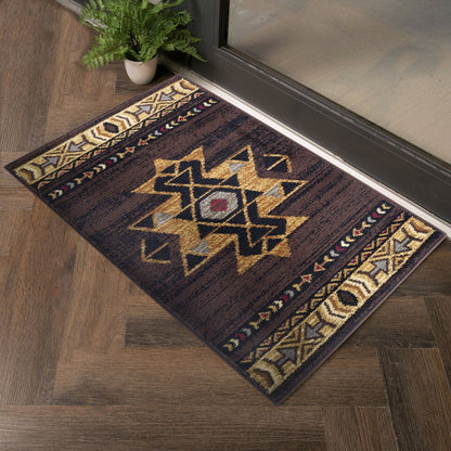 The Tribes - GC_YLS4005 Southwest Area Rug, featuring geometric patterns in brown, yellow, and black, is placed on a wooden floor near a glass door with a small potted fern nearby.