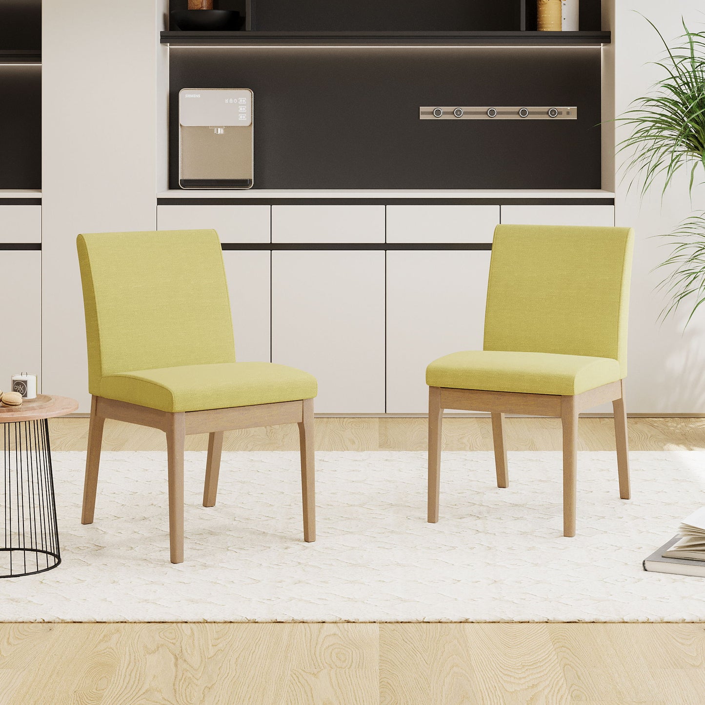 A set of two Contemporary Fabric Comfort Dining Chairs in light green with wooden legs sit on a cream rug in a modern room featuring light wood floors, white cabinets, a black accent wall, and a potted plant.