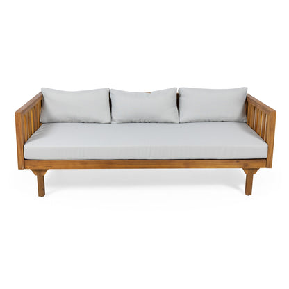 The Claremont 3 Seater Daybed features a teak acacia wood frame with slatted armrests, light gray water-resistant seat and back cushions, and three matching back pillows, shown against a white background.